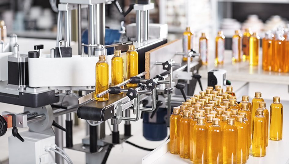 Horizontal shot of cosmetics or pharmacy plant with automated equipment. Transparent plastic bottles filled with yellow substance standing on desk and conveyor line, ready for transportation Horizontal shot of cosmetics or pharmacy plant with automated equipment. Transparent plastic bottles filled with yellow substance standing on desk and conveyor line, ready for transportation